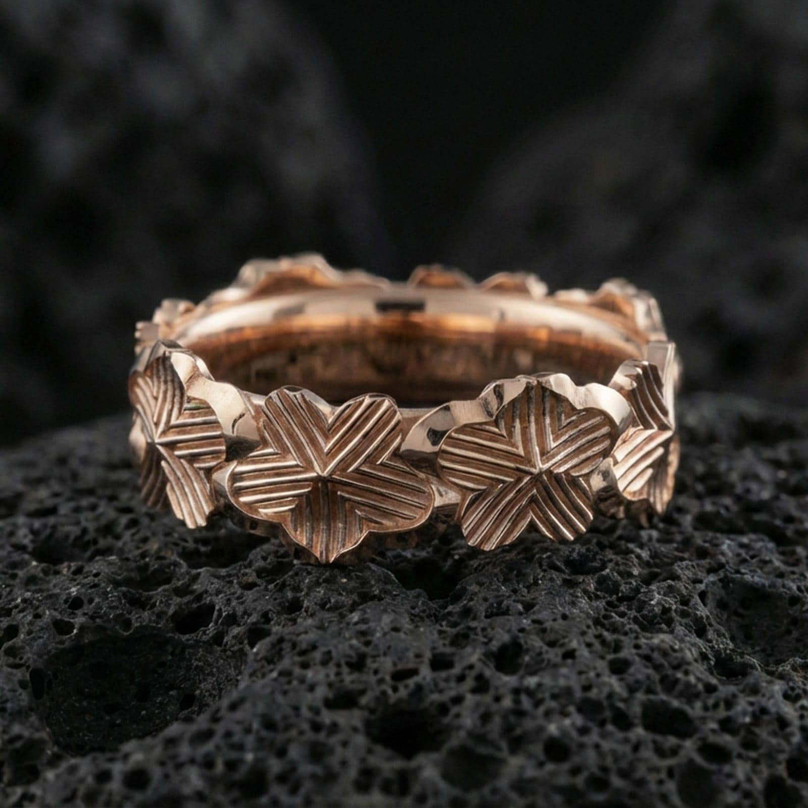 Rose gold plated floral band ring on textured volcanic rock, centered studio-style close-up showcasing soft rosy glow and intricate floral engraving with a refined finish.