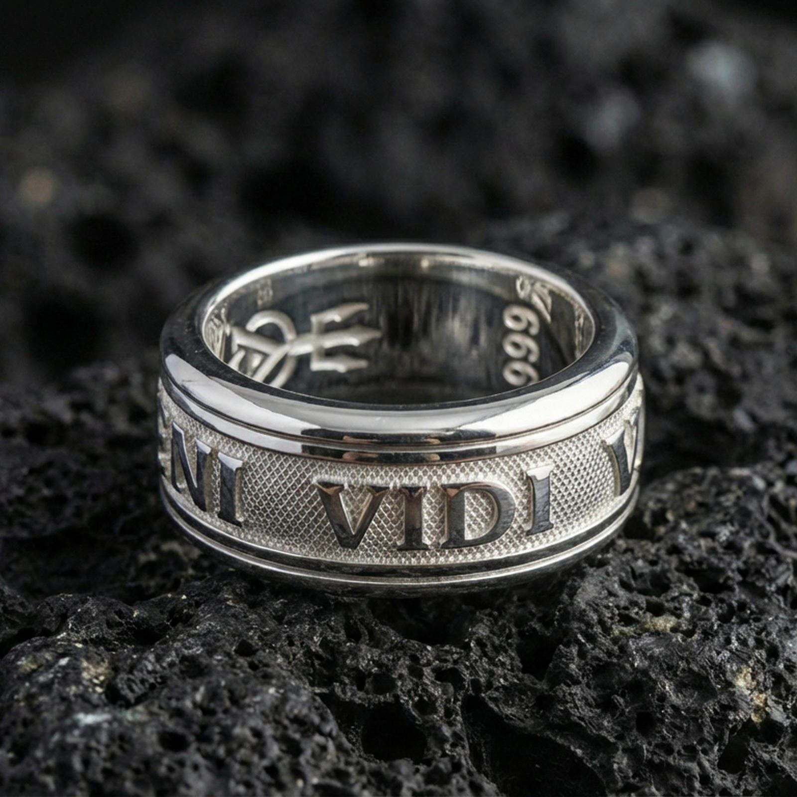 Polished silver Veni Vidi Vici spinner ring on textured volcanic rock, crisp macro product photo emphasizing clean edges, sharp engraved text, and bright reflective highlights on the spinning center.