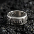 Load image into Gallery viewer, Oxidized Veni Vidi Vici spinner ring on textured volcanic rock, centered close-up highlighting the rotating band, raised Latin lettering, and deep antique shadowed contrast.
