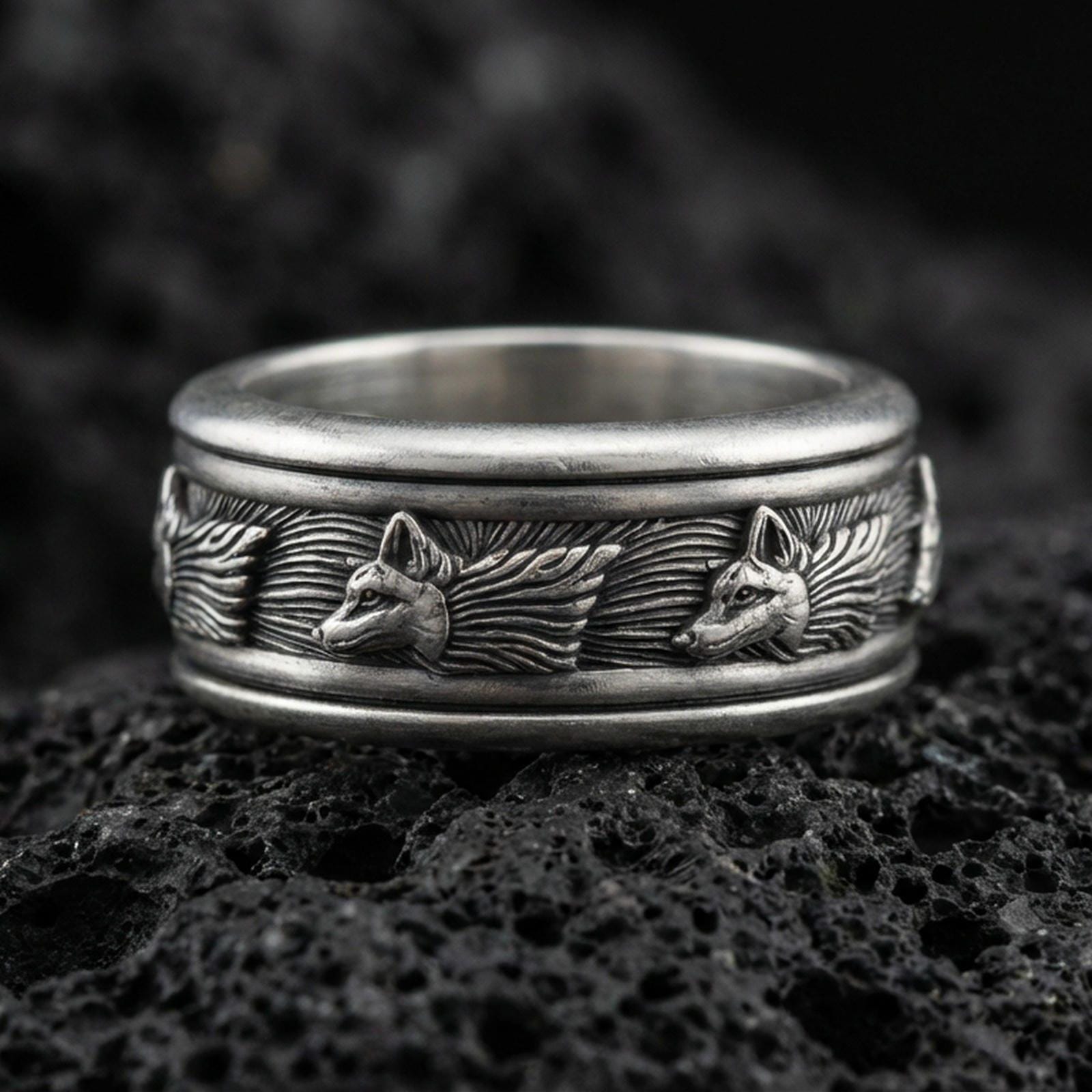 Oxidized wolf head band ring on textured volcanic rock, centered close-up highlighting the carved wolf motifs, flowing fur texture, and deep antique shadowed contrast.