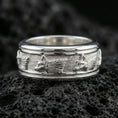 Load image into Gallery viewer, Polished silver wolf head band ring on textured volcanic rock, crisp macro product photo emphasizing clean edges, sharp wolf relief, and bright reflective highlights across the textured band.
