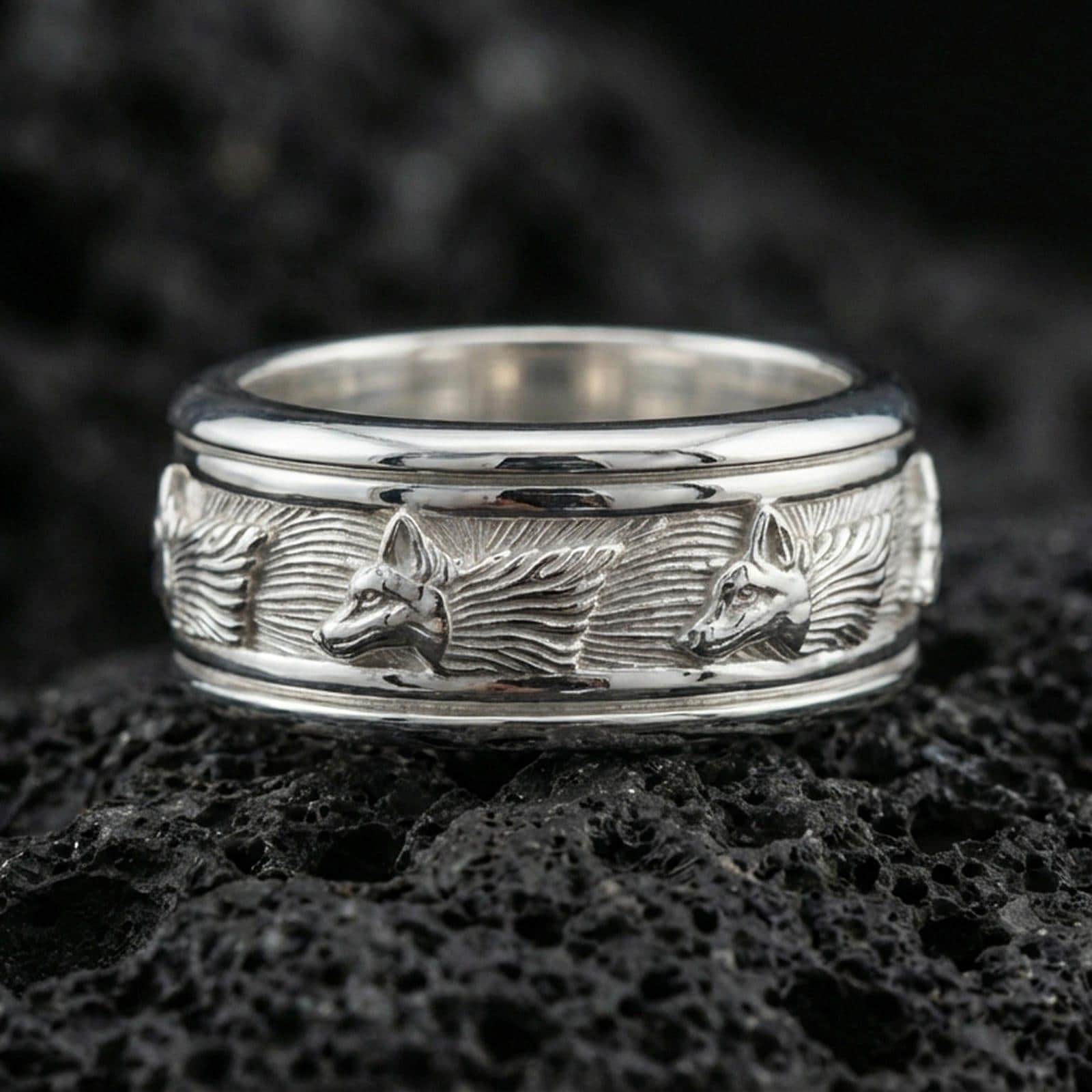 Polished silver wolf head band ring on textured volcanic rock, crisp macro product photo emphasizing clean edges, sharp wolf relief, and bright reflective highlights across the textured band.