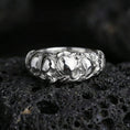 Load image into Gallery viewer, Polished silver skull band ring on textured volcanic rock, crisp macro product photo emphasizing clean edges, sharp skull detailing, and bright reflective highlights across the band.
