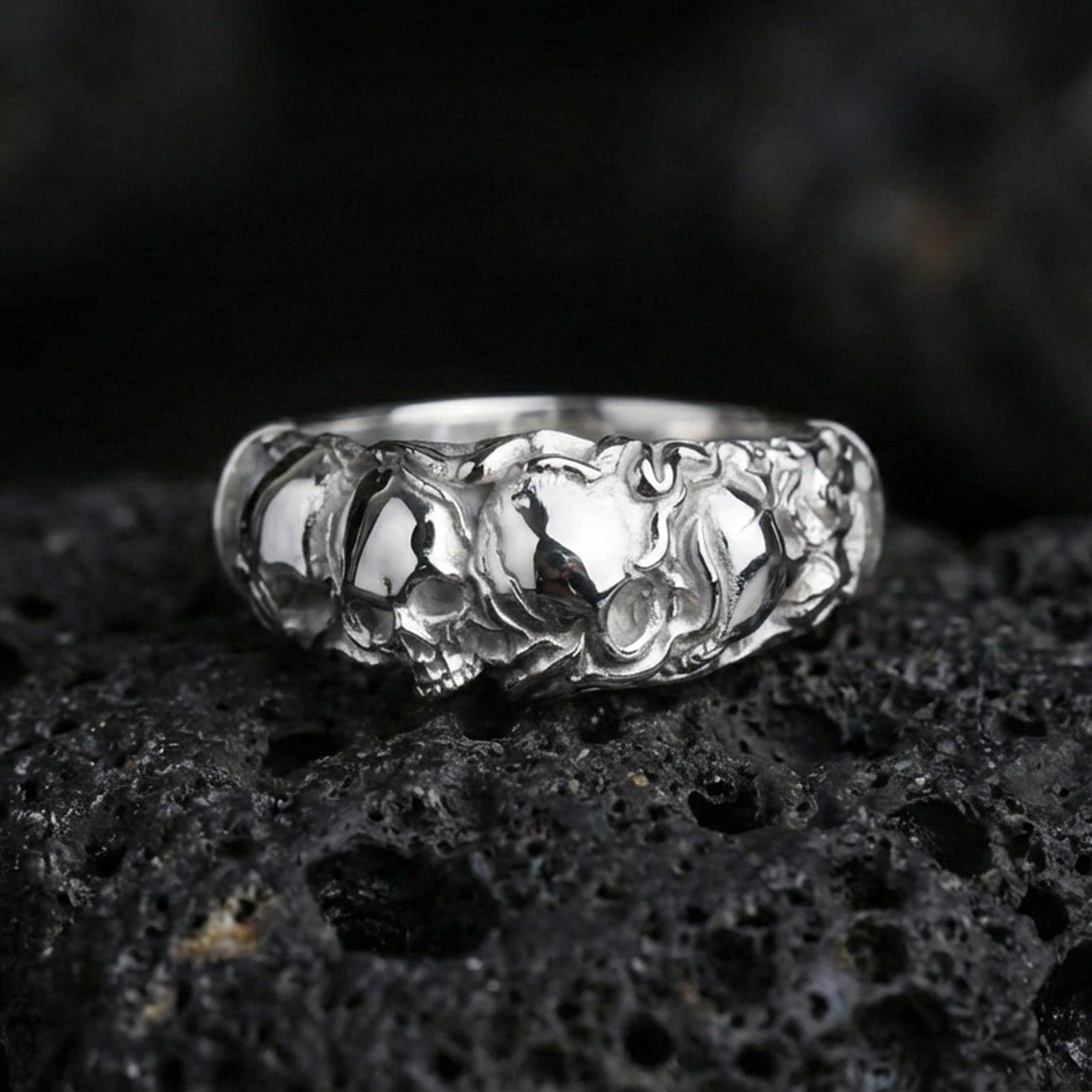 Polished silver skull band ring on textured volcanic rock, crisp macro product photo emphasizing clean edges, sharp skull detailing, and bright reflective highlights across the band.