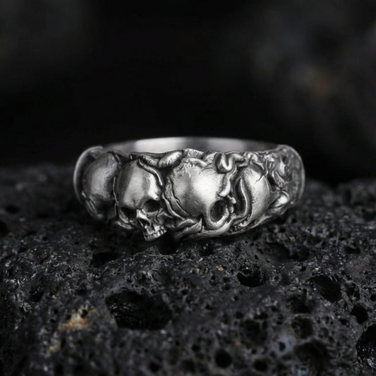 Oxidized skull band ring on textured volcanic rock, centered close-up highlighting the raised skull row, sculpted contours, and deep antique shadowed contrast.