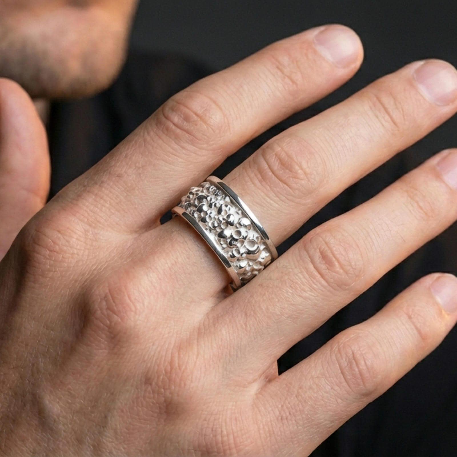Polished silver skull cuff ring worn on a finger, clean lifestyle wear shot capturing bright shine and the detailed skull texture in natural light.