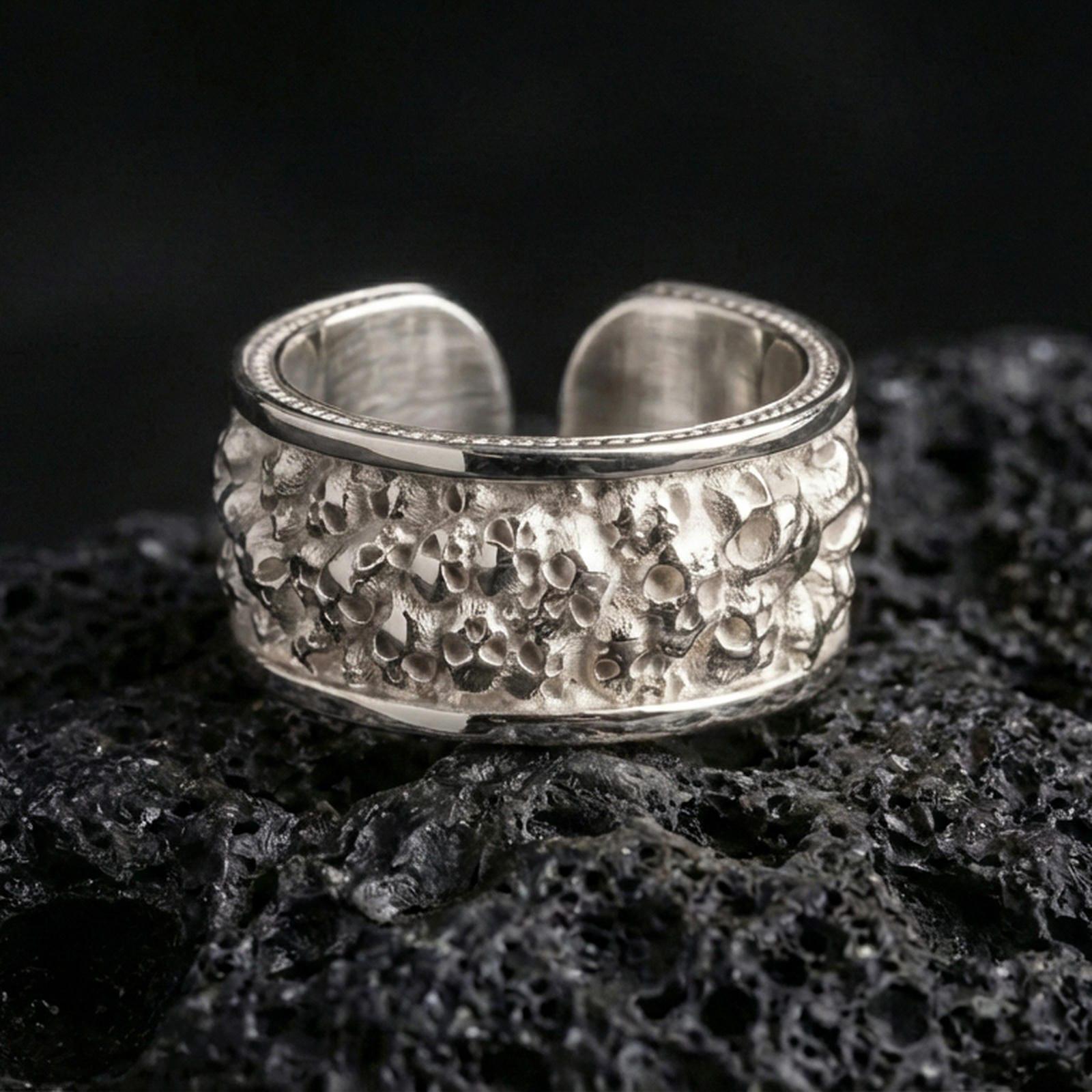 Polished silver skull cuff ring on textured volcanic rock, crisp macro product photo emphasizing clean edges, sharp skull detailing, and bright reflective highlights across the open band.
