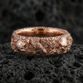 Load image into Gallery viewer, Gold plated skull and koi floral band ring on textured volcanic rock, premium close-up with warm reflective shine across the skull motifs, koi detailing, and raised ornamental contours.
