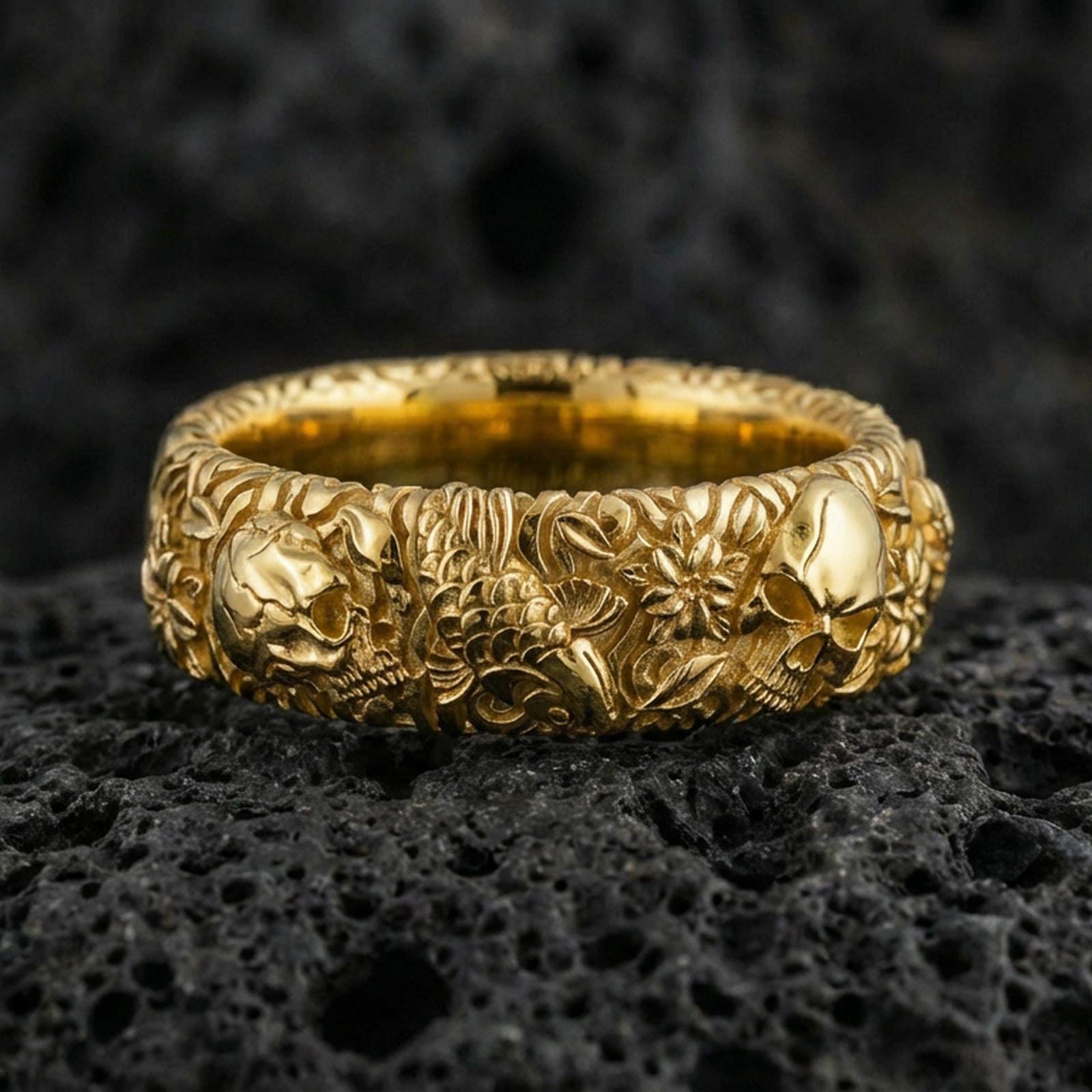 Rose gold plated skull and koi floral band ring on textured volcanic rock, centered studio-style close-up showcasing soft rosy glow and intricate skull-and-koi floral detailing with a refined finish.