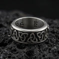 Load image into Gallery viewer, Oxidized Celtic triquetra band ring on textured volcanic rock, centered close-up highlighting the repeating Trinity knot pattern and deep antique shadowed contrast.
