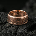 Load image into Gallery viewer, Rose gold plated Egyptian symbols band ring on textured volcanic rock, centered studio-style close-up showcasing soft rosy glow and crisp hieroglyph detailing with a refined finish.
