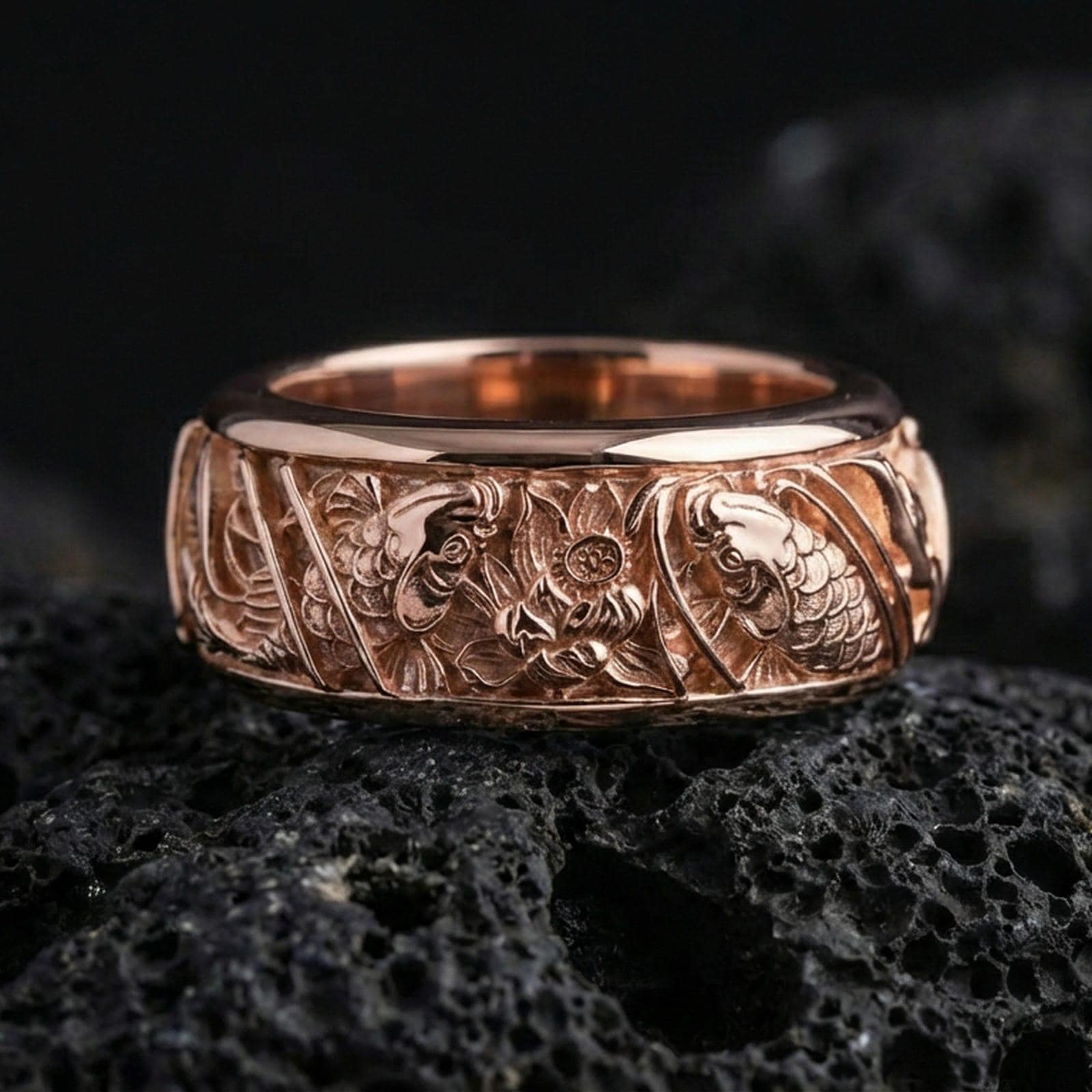 Rose gold plated koi fish and lotus band ring on textured volcanic rock, centered studio-style close-up showcasing soft rosy glow and intricate koi-and-lotus detailing with a refined finish.