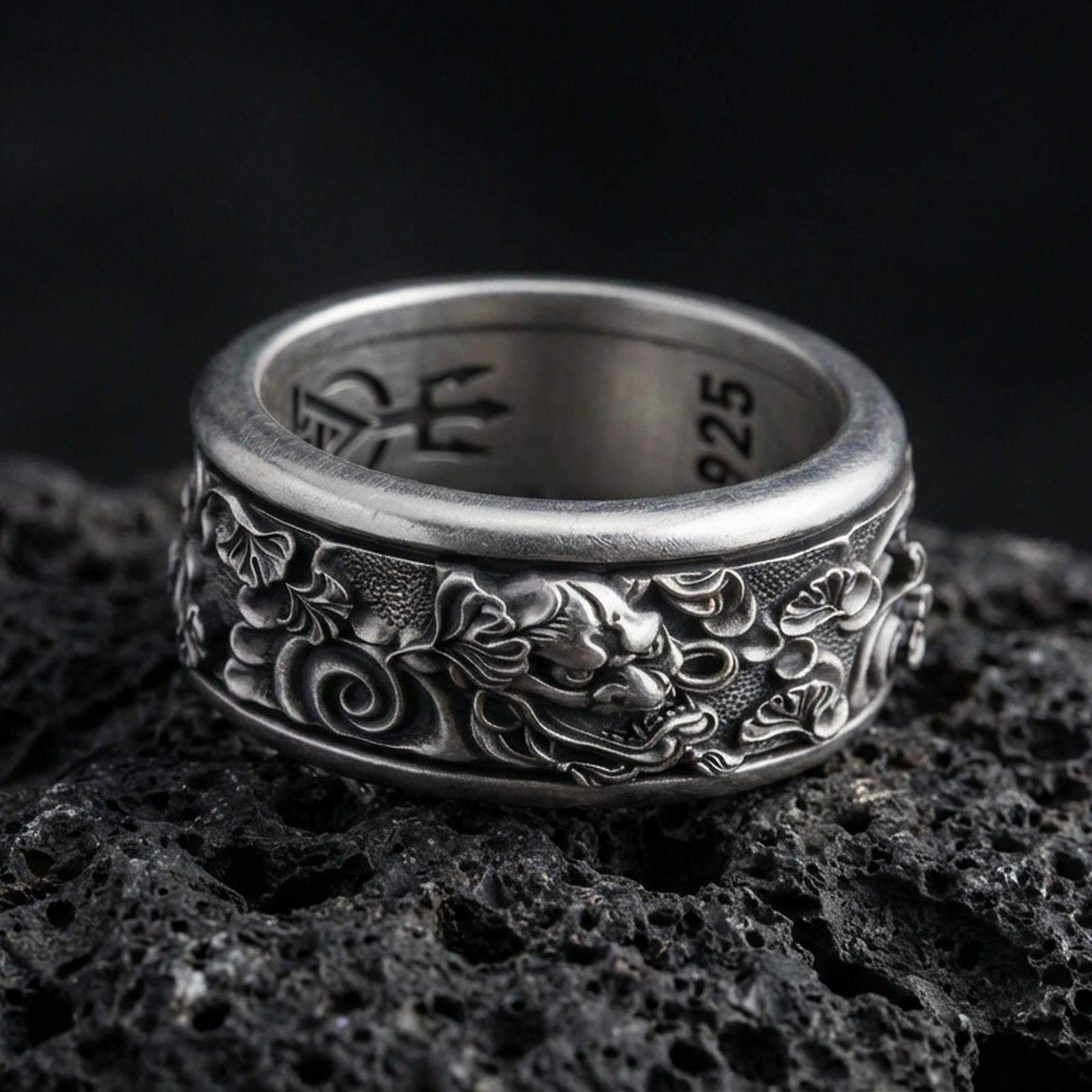 Oxidized oriental dragon band ring on textured volcanic rock, centered close-up highlighting the fierce dragon head relief, swirling cloud motifs, and deep antique shadowed contrast.