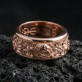 Load image into Gallery viewer, Rose gold plated oriental dragon band ring on textured volcanic rock, centered studio-style close-up showcasing soft rosy glow and intricate dragon-and-cloud detailing with a refined finish.
