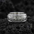 Load image into Gallery viewer, Polished silver twin lion band ring on textured volcanic rock, crisp macro product photo emphasizing clean edges, sharp mane engraving, and bright reflective highlights across the sculpted lions.
