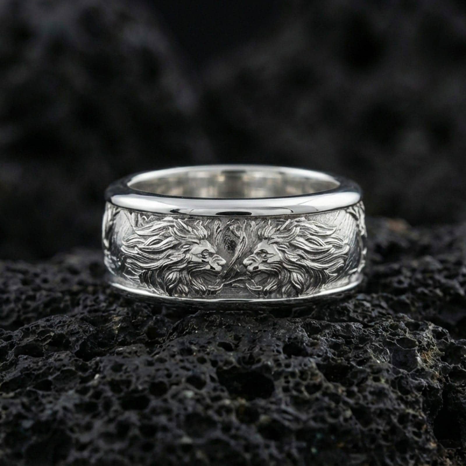 Polished silver twin lion band ring on textured volcanic rock, crisp macro product photo emphasizing clean edges, sharp mane engraving, and bright reflective highlights across the sculpted lions.