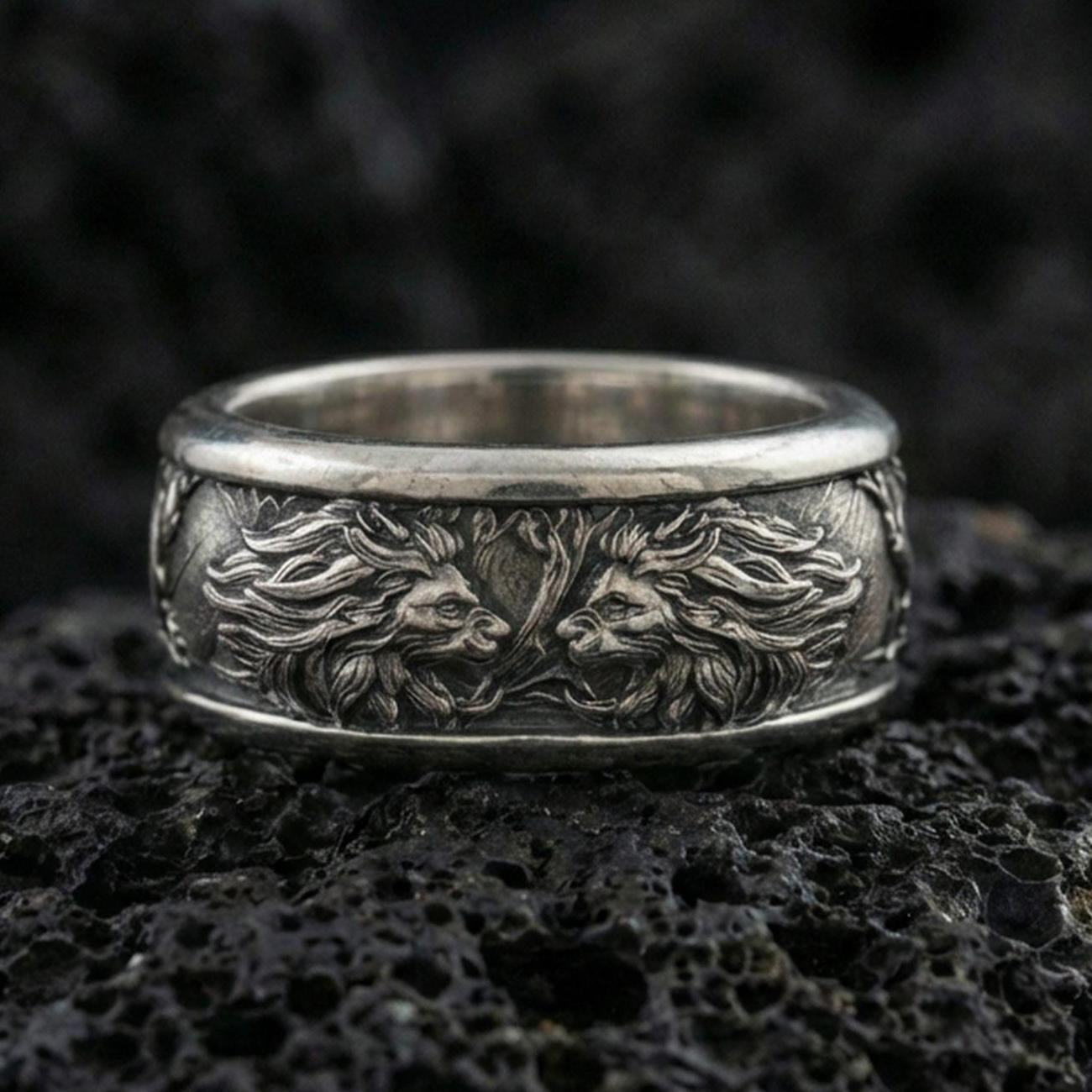 Oxidized twin lion band ring on textured volcanic rock, centered close-up highlighting the facing lion heads, flowing mane relief, and deep antique shadowed contrast.