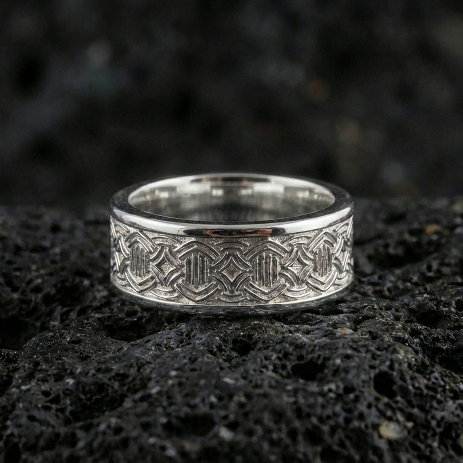 Polished silver geometric knotwork band ring on textured volcanic rock, crisp macro product photo emphasizing clean edges, sharp engraved lines, and bright reflective highlights across the band.