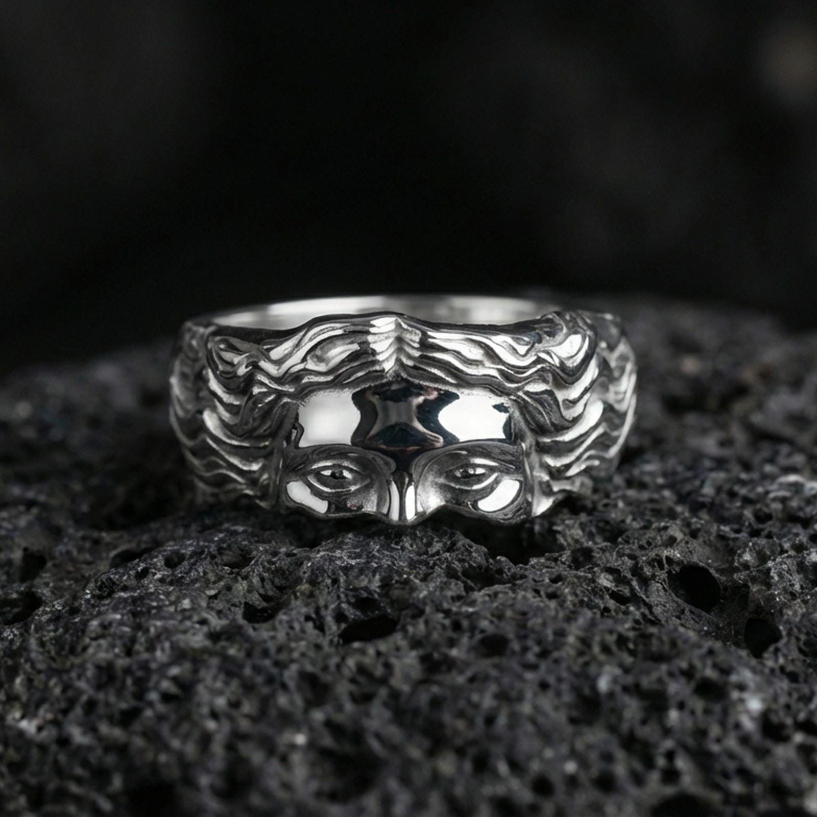 Polished silver face relief band ring on textured volcanic rock, crisp macro product photo emphasizing clean edges, smooth facial contours, and bright reflective highlights across the sculpted surface.