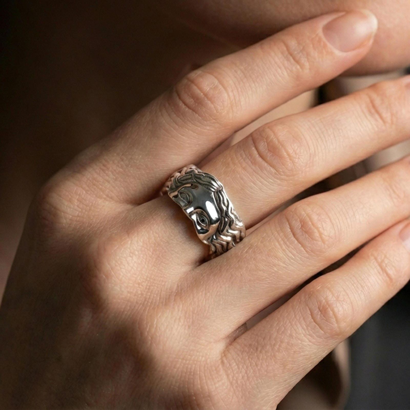 Polished silver face relief band ring worn on a finger, clean lifestyle wear shot capturing bright shine and the detailed face relief in natural light.