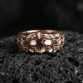Load image into Gallery viewer, Rose gold plated face relief band ring on textured volcanic rock, centered studio-style close-up showcasing soft rosy glow and crisp facial sculpting with a refined finish.
