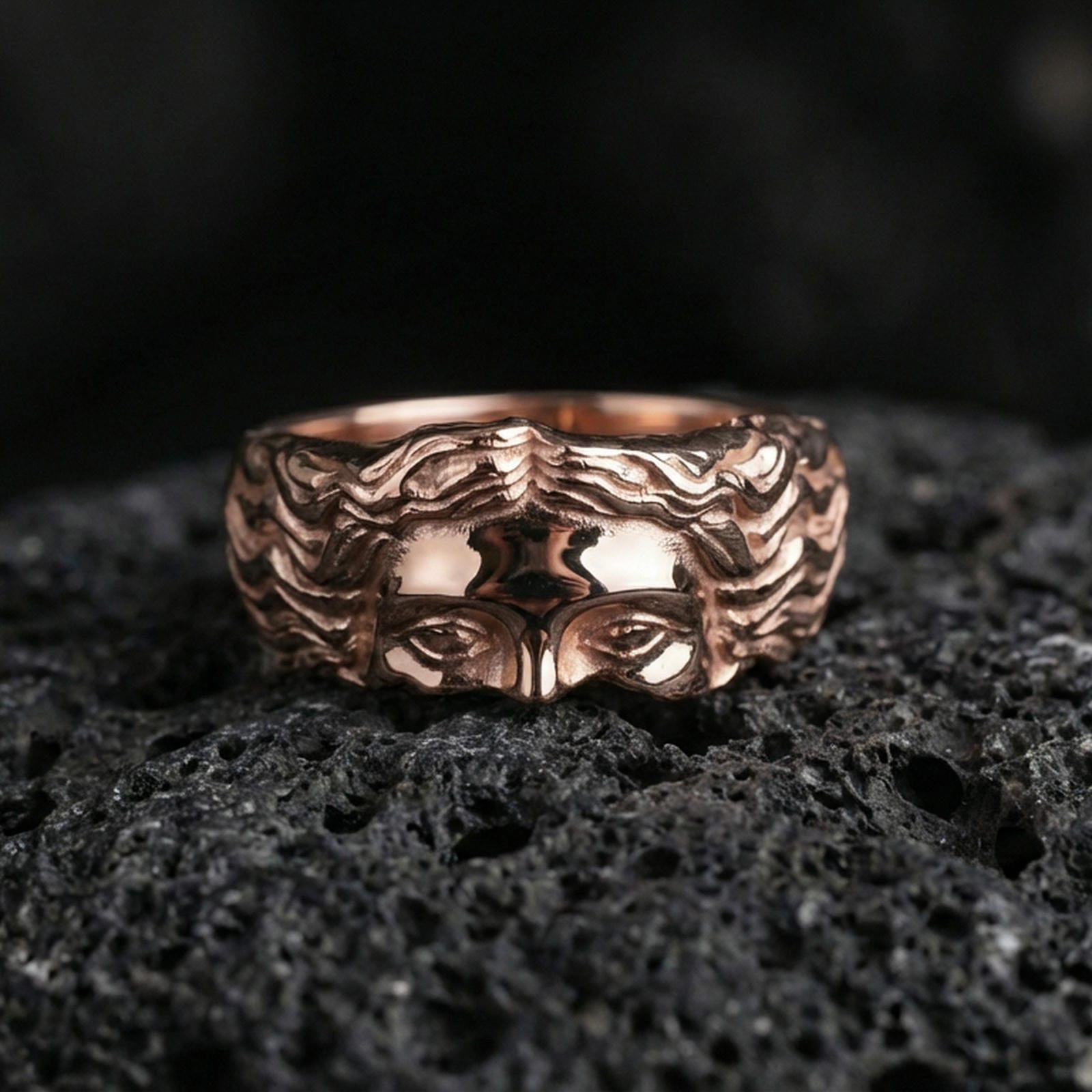Rose gold plated face relief band ring on textured volcanic rock, centered studio-style close-up showcasing soft rosy glow and crisp facial sculpting with a refined finish.