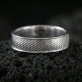 Load image into Gallery viewer, Polished silver diagonal groove band ring on textured volcanic rock, crisp macro product photo emphasizing clean edges, sharp diagonal lines, and bright reflective highlights across the band.
