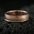 Load image into Gallery viewer, Rose gold plated diagonal groove band ring on textured volcanic rock, centered studio-style close-up showcasing soft rosy glow and crisp diagonal line detailing with a refined finish.
