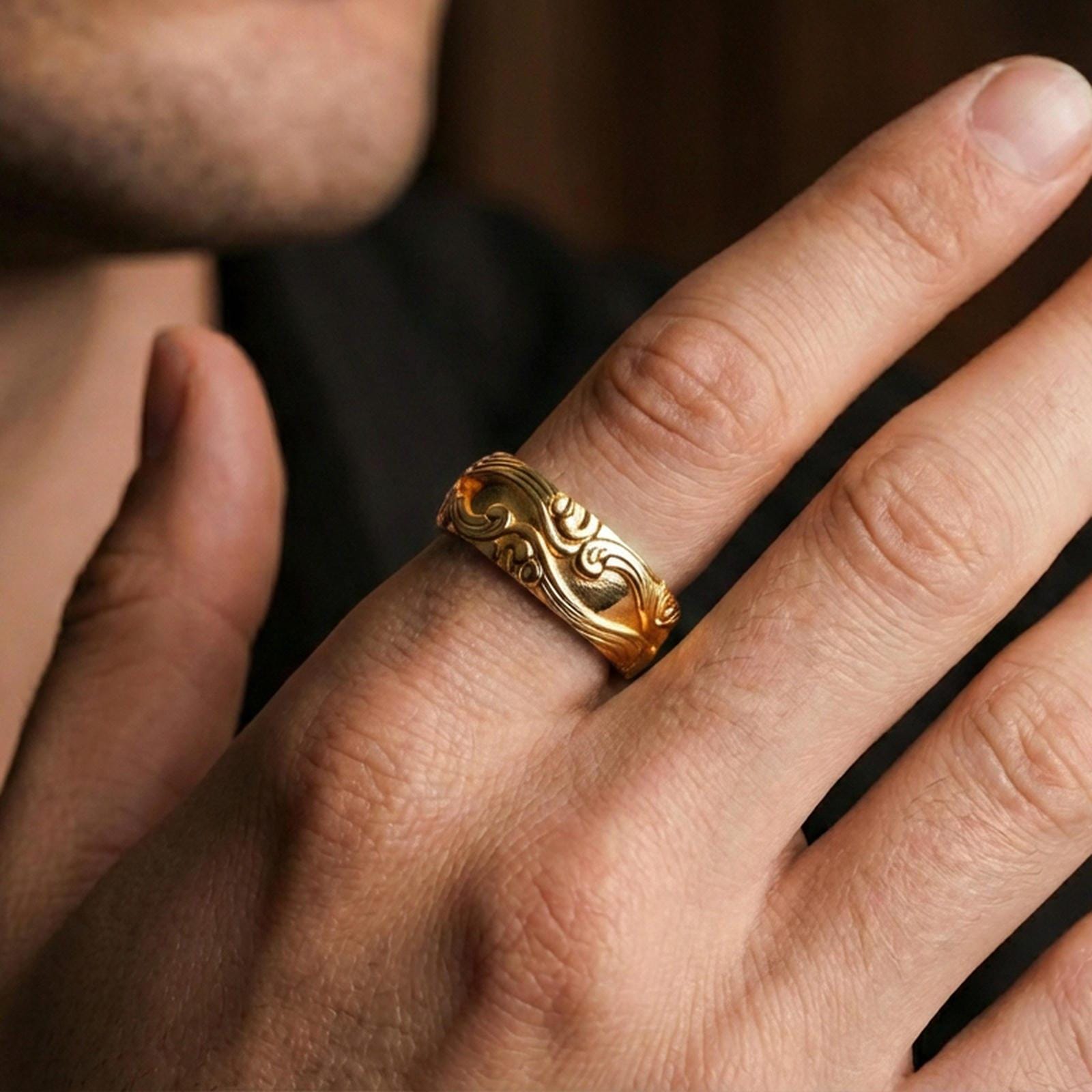 Gold plated scrollwork band ring worn on a finger, lifestyle image with warm shine and clear visibility of the raised swirling patterns.