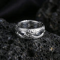 Load image into Gallery viewer, Polished silver scrollwork band ring on textured volcanic rock, crisp studio macro emphasizing clean reflective edges and the carved swirl relief.
