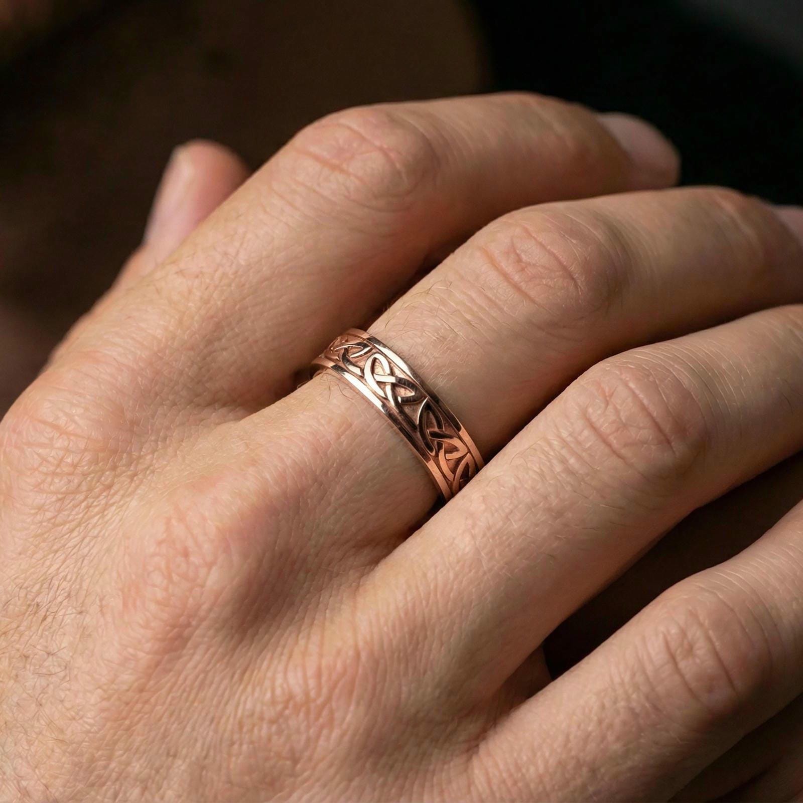 Rose gold plated Celtic knot band ring worn on a finger, lifestyle wear shot featuring elegant rosy sheen and close detail of the Celtic knot motif.