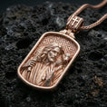 Load image into Gallery viewer, Rose gold plated religious Jesus pendant with shepherd figure, lamb motif, and framed sacred design resting on volcanic rock in an elegant close-up product presentation
