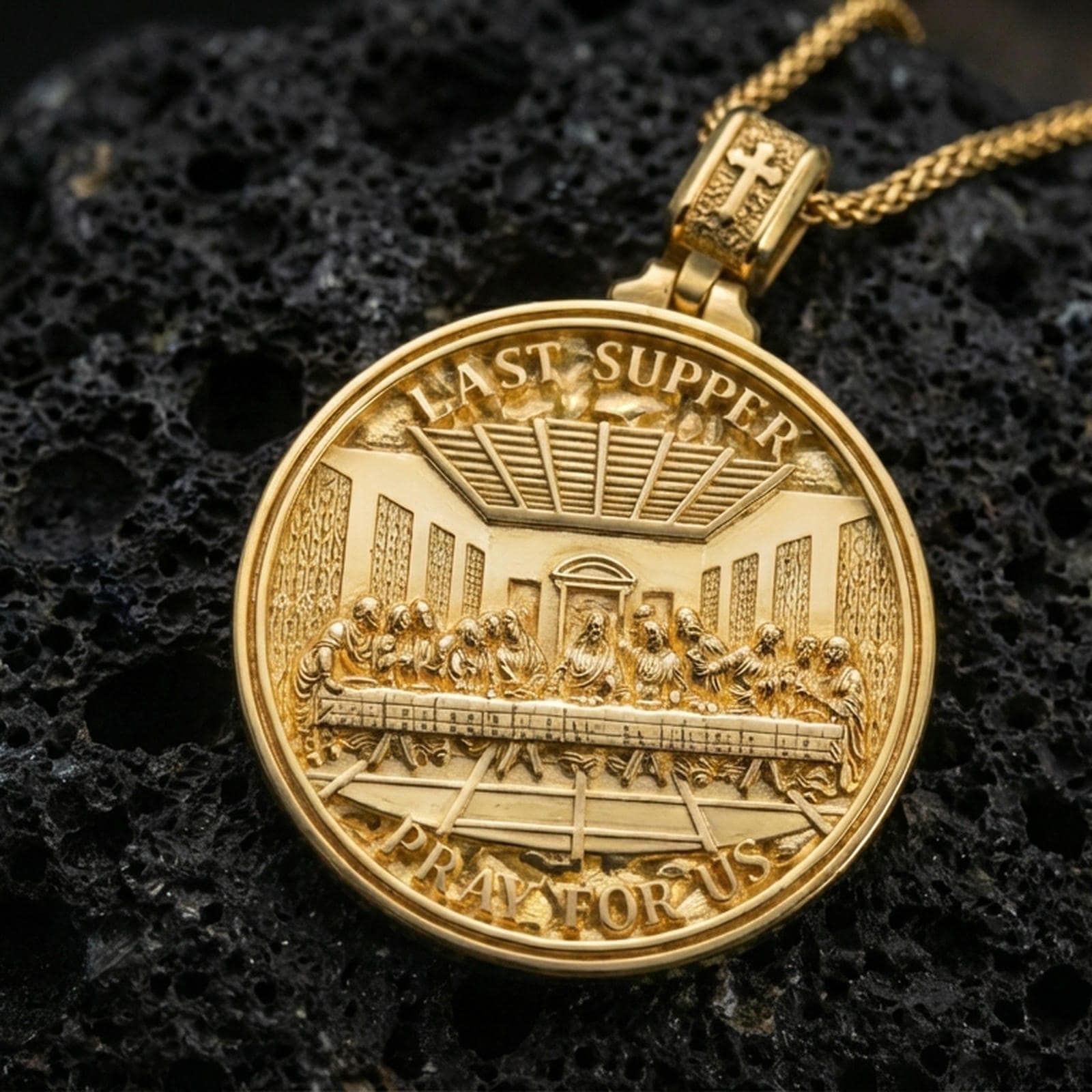 Gold plated round religious medallion with Last Supper scene, Pray for Us text, and engraved prayer detail showcased on black volcanic rock in a refined macro jewelry image