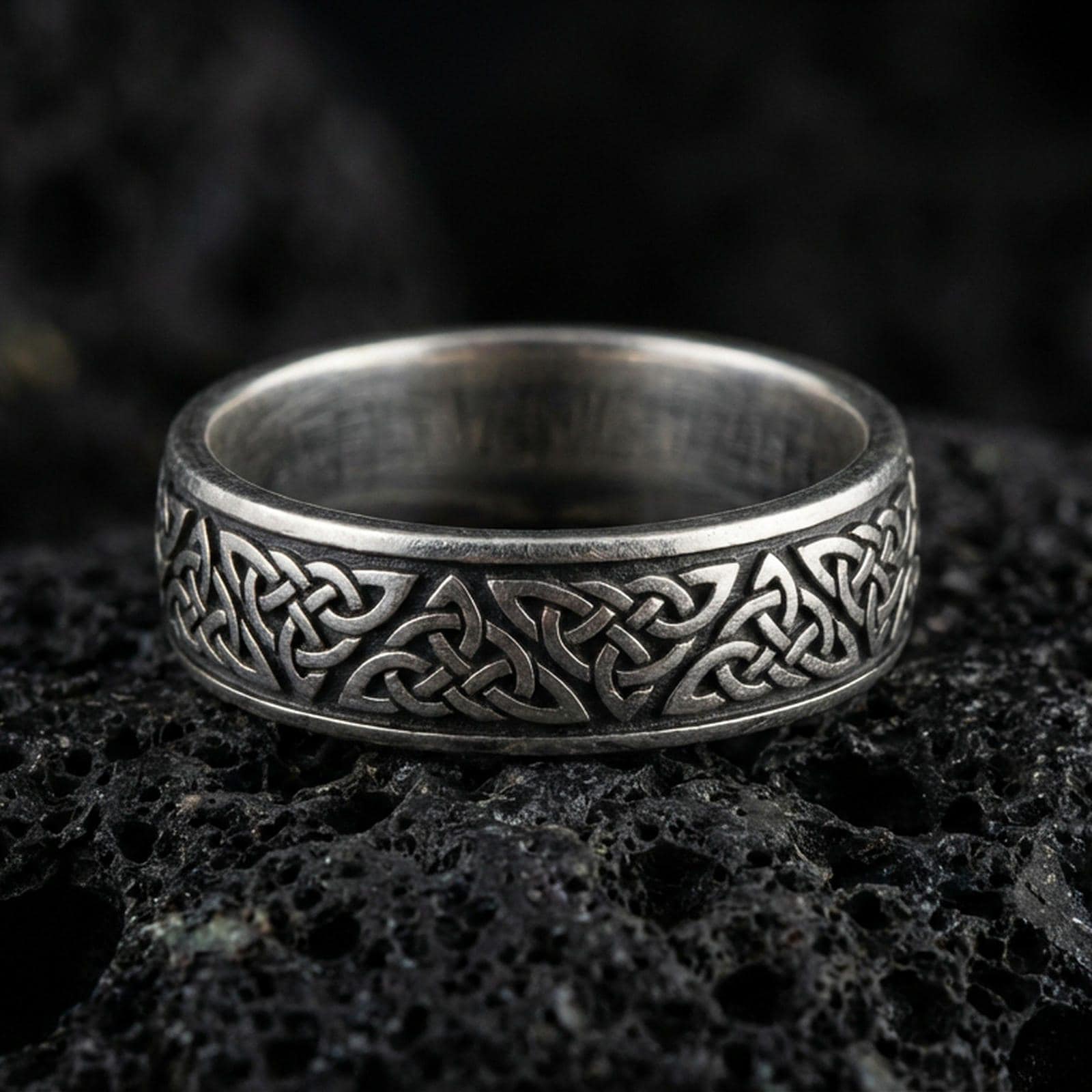 Oxidized Celtic knot band ring on volcanic stone, macro close-up highlighting the darkened recesses and raised interlaced knotwork detail.