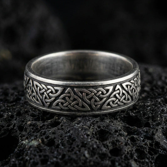 Oxidized Celtic knot band ring on volcanic stone, macro close-up highlighting the darkened recesses and raised interlaced knotwork detail.