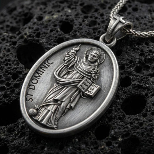 Oxidized Saint Dominic pendant with haloed saint figure, book detail, and St Dominic inscription displayed on dark volcanic rock in a close-up luxury jewelry composition