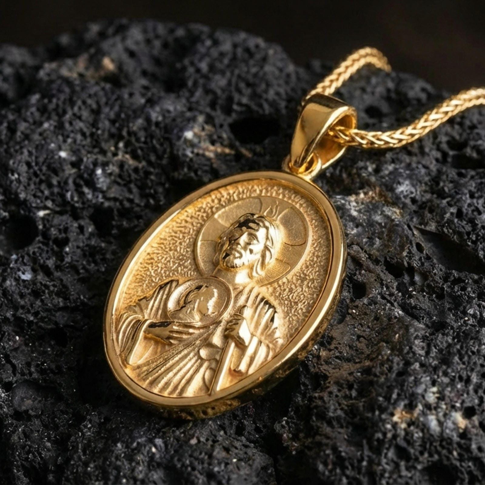 Gold plated Saint Jude pendant with detailed saint figure, round medallion motif, and classic religious symbolism showcased on black volcanic rock in a refined macro jewelry image