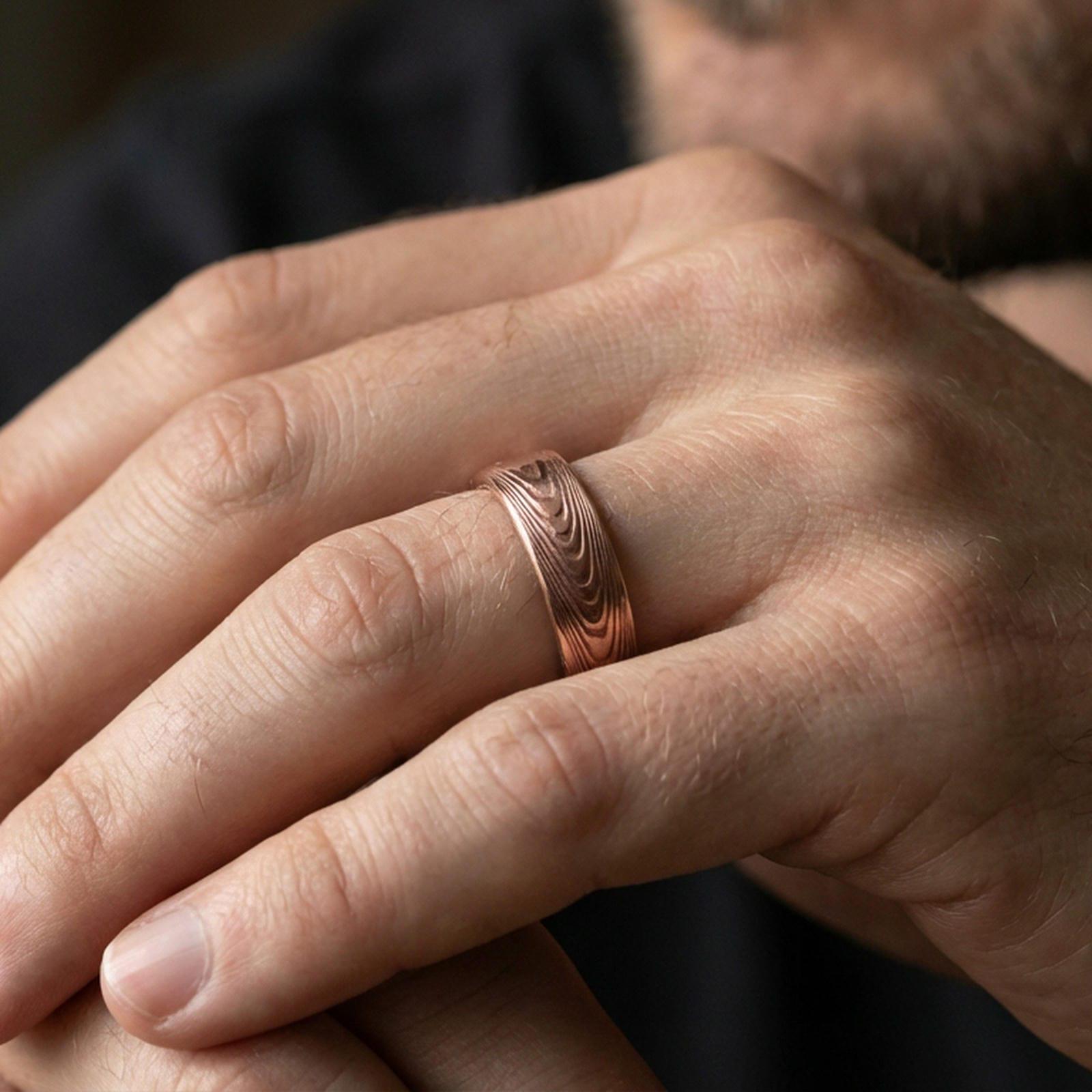 Rose gold plated Damascus-style band ring worn on a finger, lifestyle wear photo with elegant rosy tone and distinct Damascus wave detailing.
