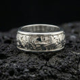 Load image into Gallery viewer, Polished silver hieroglyph band ring on volcanic stone, crisp macro product photo emphasizing clean engraved glyph details and bright reflective edges.
