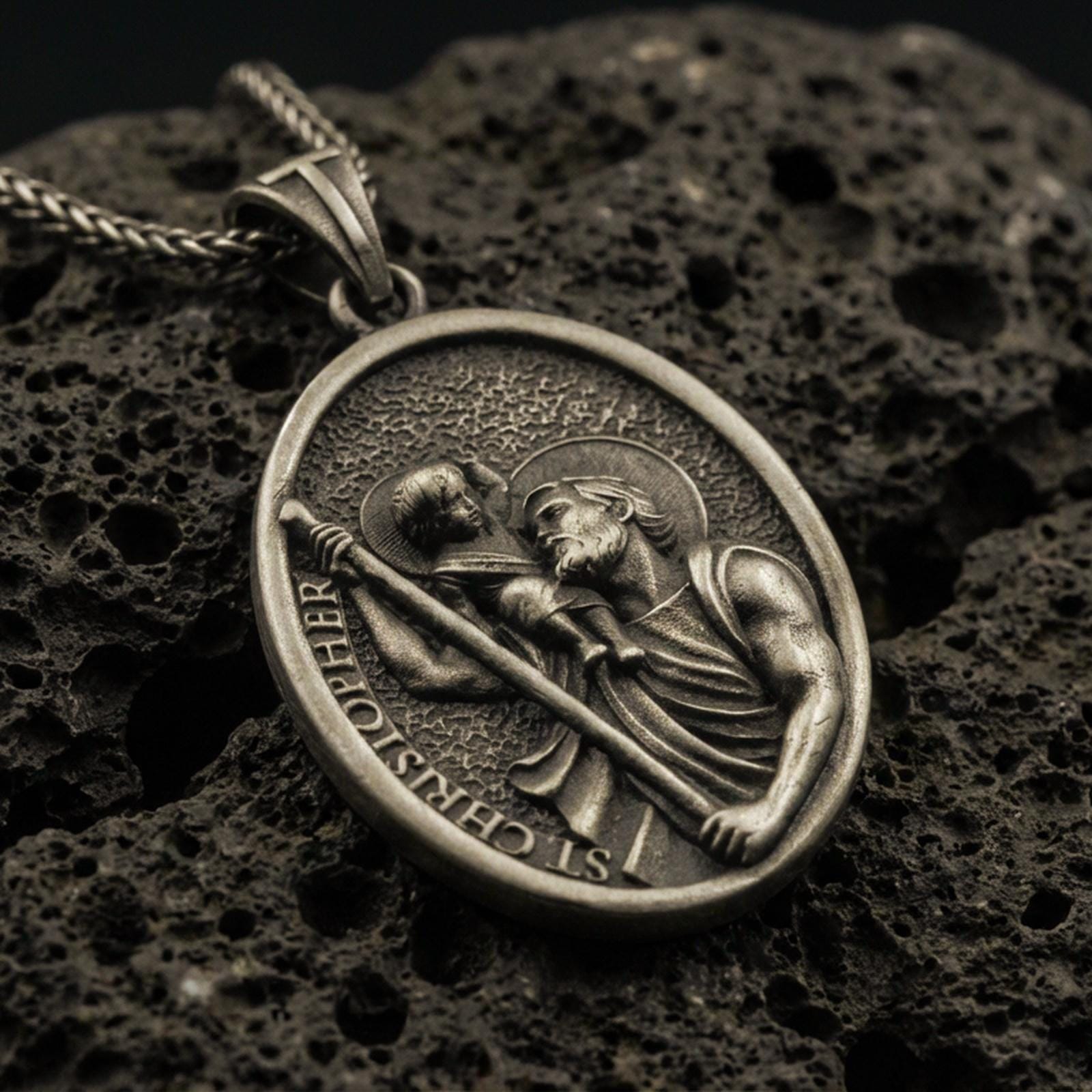 Bronze Saint Christopher pendant with Child Jesus, staff detail, and oval devotional portrait displayed on dark volcanic rock in a close-up luxury jewelry composition