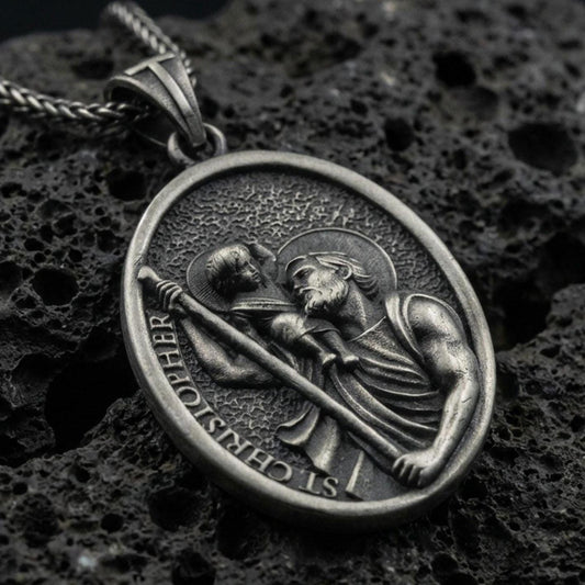 Oxidized Saint Christopher pendant with Child Jesus, staff detail, and oval devotional portrait displayed on dark volcanic rock in a close-up luxury jewelry composition