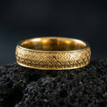 Load image into Gallery viewer, Gold plated fleur-de-lis band ring on volcanic stone, premium close-up showing warm gold tone across the repeating fleur-de-lis texture.
