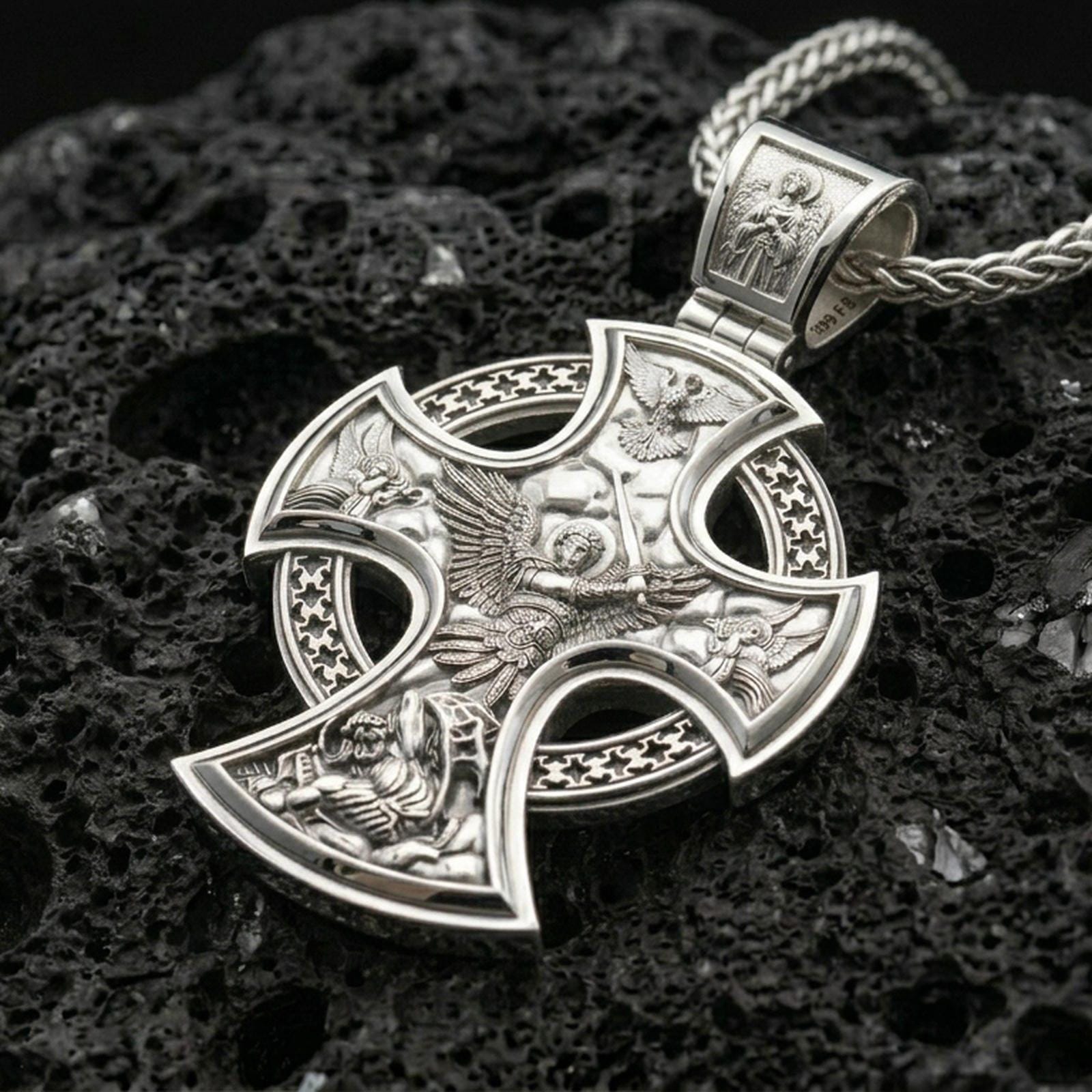 Polished silver Archangel Michael pendant with ornate cross frame, angel warrior relief, and intricate religious scene placed on textured volcanic rock in a premium studio product shot
