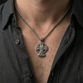 Load image into Gallery viewer, Oxidized Saint Michael cross pendant with winged archangel scene worn on the neck in a lifestyle jewelry shot, styled against the chest for a bold and protective look
