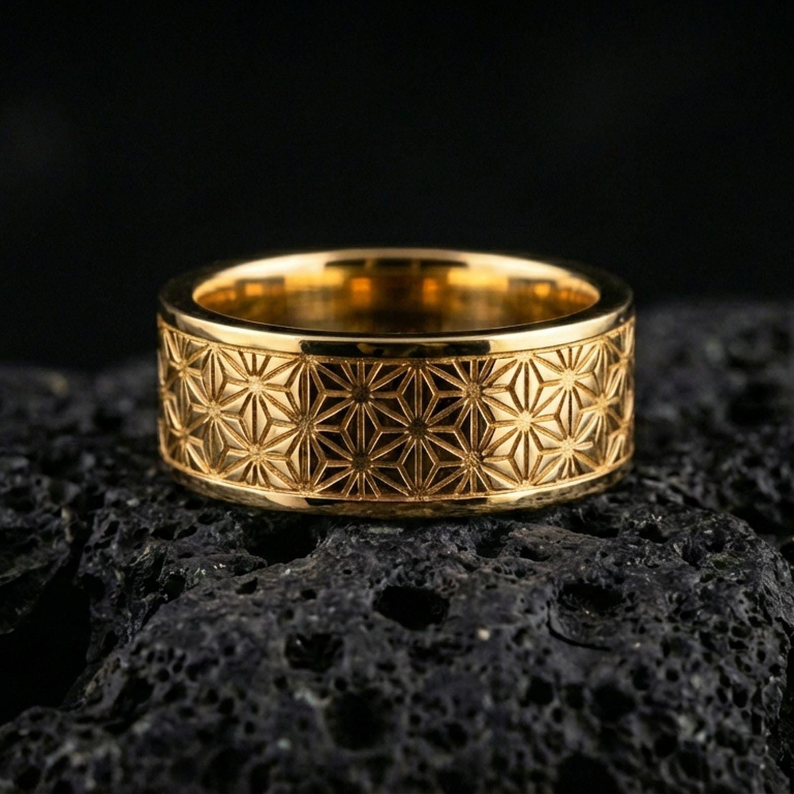 Gold plated geometric floral band ring on volcanic stone, premium close-up showing warm gold tone across the engraved Japanese-inspired pattern.