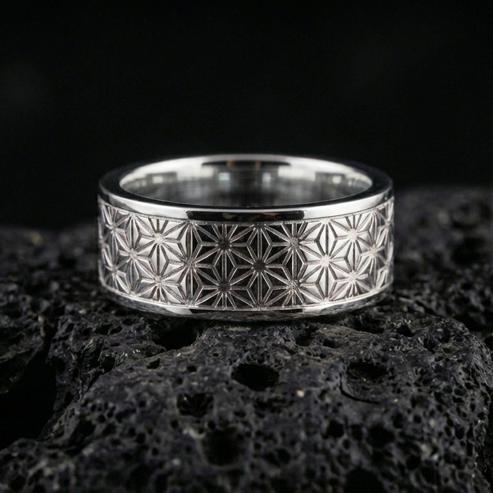 Polished silver geometric floral band ring on volcanic stone, clean product photo emphasizing the sharp repeating star-flower grid and reflective surface.