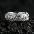 Load image into Gallery viewer, Polished silver scrollwork band ring on volcanic stone, clean product photo emphasizing bright shine and crisp ornamental curls.

