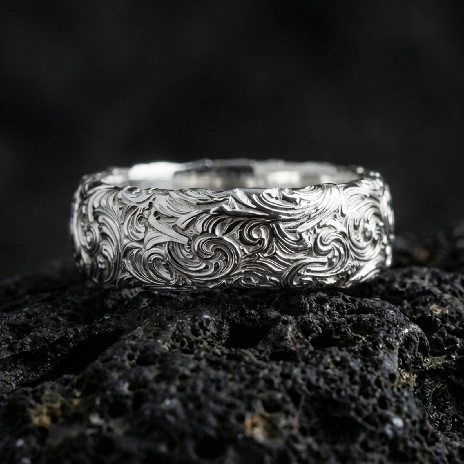 Polished silver scrollwork band ring on volcanic stone, clean product photo emphasizing bright shine and crisp ornamental curls.