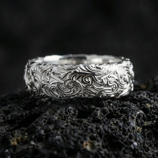 Polished silver scrollwork band ring on volcanic stone, clean product photo emphasizing bright shine and crisp ornamental curls.