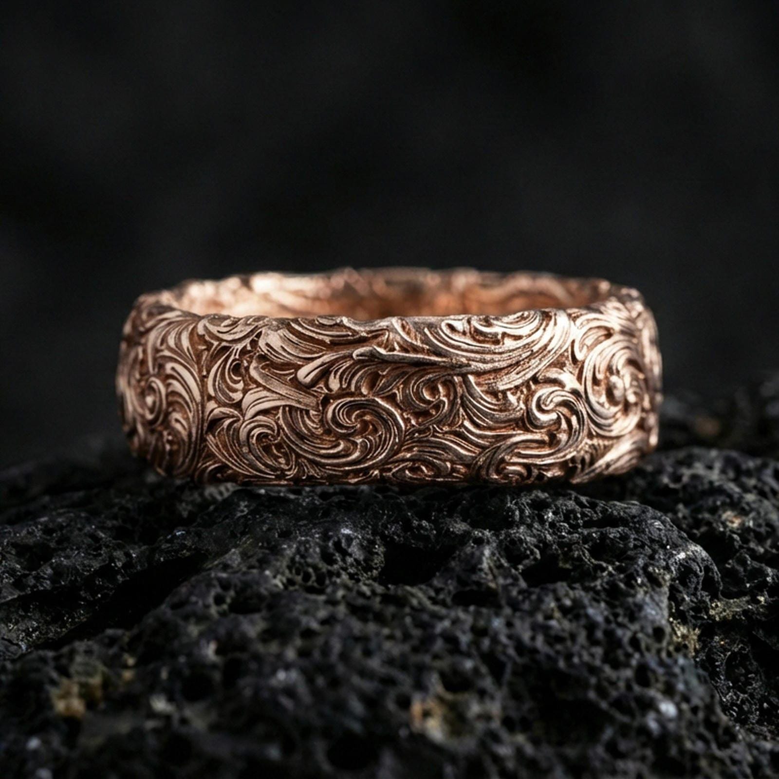 Rose gold plated scrollwork band ring on volcanic stone, refined close-up featuring soft rose highlights and ornate swirling pattern depth.
